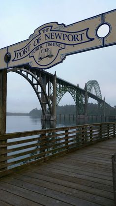 the port of newport sign is hanging over the water's edge near a bridge