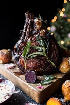 a large roast beef on a cutting board next to other food and christmas tree in the background