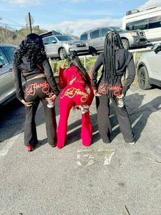 three women with dreadlocks are standing in front of some parked cars and one is bending over