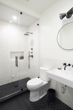 a white toilet sitting next to a walk in shower under a round mirror on the wall