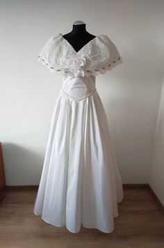 a white dress on a mannequin stand in front of a wall and wooden floor