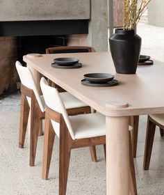 a wooden table with white chairs and a black vase on top of it next to a fire place