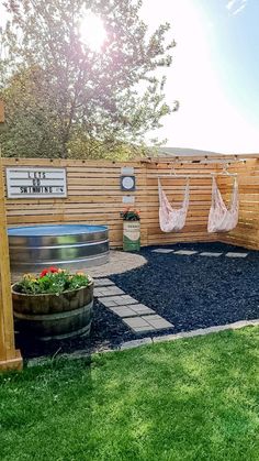 a backyard with a hammock and potted plants on the grass, next to a wooden fence