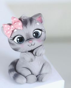 a gray cat with a pink bow sitting on top of a white box and looking at the camera