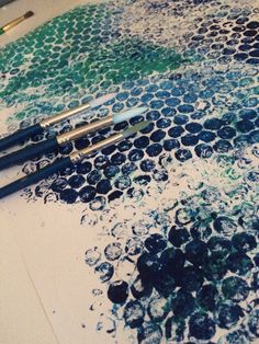 three paint brushes are sitting on top of a piece of paper that is covered in blue and green circles