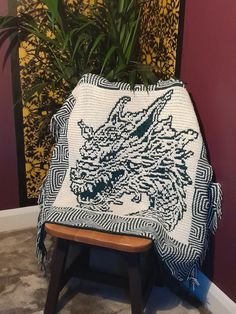 a white and black blanket sitting on top of a wooden stool next to a potted plant