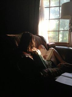 a person sitting on a couch with a book in their lap and sunlight coming through the window