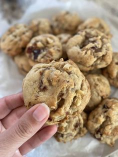 a hand holding a chocolate chip cookie over a pile of other cookies on wax paper