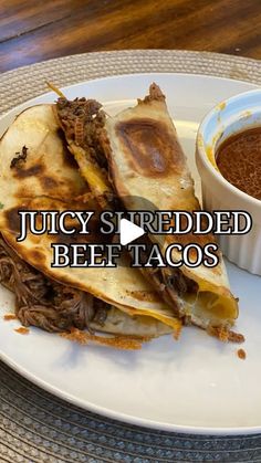 juicy shredded beef tacos on a white plate with a bowl of chili and sauce