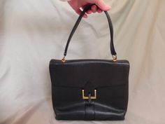 "Classy black leather handbag with black leather handle, modern brass clasp and brass feet on the bottom.  The center vertical part of the clasp swings to the left or the right to release the square brass piece when opening the bag. The lining is part black vinyl and part black leather. There are two open pockets and one zippered pocket in the roomy interior. It looks like the brand name has been worn off, but the words \"Macy Associates\" are stamped on the inside in gold as well as \"Made in F French Handbags, Black Leather Handbag, Modern Mid Century, Black Leather Handbags, How To Make Handbags, Black Vinyl, Leather Handbag, Midcentury Modern, Leather Handle