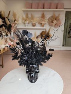 a black vase with flowers and feathers on a white table in a room filled with shelves