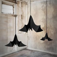 three black paper bats hanging from strings in an empty room with a radiator