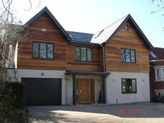 a two story house with wood siding and black garage doors on the front, surrounded by trees