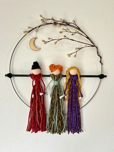 three dolls are hanging on a circular metal wall decoration with branches and moon in the background