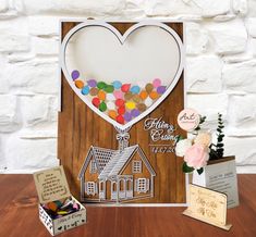 a card with a house and balloons in the shape of a heart on top of it