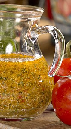 a glass pitcher filled with pesto next to tomatoes on a wooden cutting board,