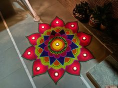 a colorful flower design on the ground with lit candles in front of it and some potted plants