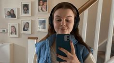 a woman wearing headphones is looking at her cell phone while standing on the stairs