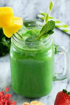 a green smoothie in a mason jar with strawberries and pineapples on the side