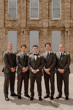 a group of men standing next to each other in front of a tall brick building