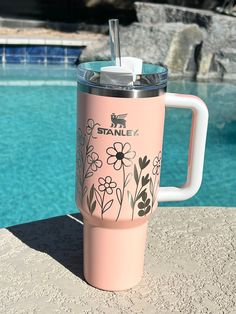 a pink tumbler cup sitting next to a swimming pool with flowers on the side