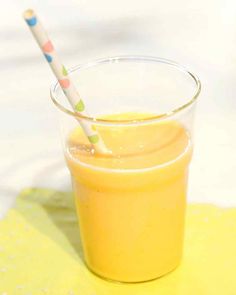 a glass filled with orange juice on top of a yellow place mat and two straws sticking out of it