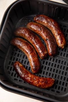 four sausages are being cooked in an air fryer