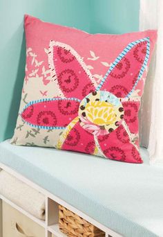 a pink flower pillow sitting on top of a white bench next to a blue wall