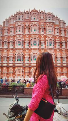 a woman in pink is standing next to a moped and looking at a large building