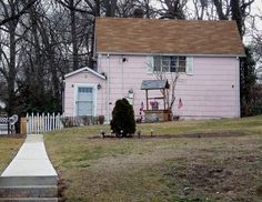 a small pink house with a white picket fence and trees in the backgroud