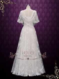 a white wedding dress on display in front of a purple wall with an ornate frame