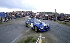 a blue car driving down a dirt road in front of a crowd