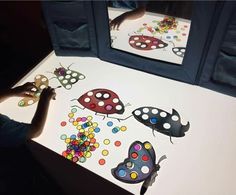 a child's hand is drawing on the table with colored dots and ladybugs