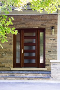 the front door is made of wood and has glass panels on each side, along with a brick wall