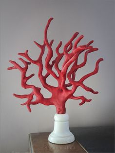 a red coral sculpture sitting on top of a wooden table next to a white vase