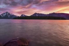 the sun is setting over some mountains in the distance, with water and rocks on the shore