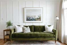 a green velvet couch with white pillows in a living room next to a painting on the wall