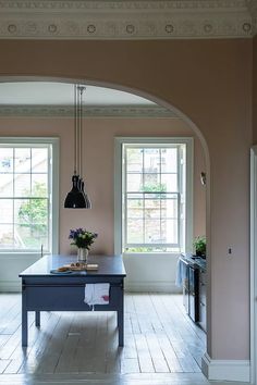 a kitchen with pink walls and white floors, an island table in the center is flanked by two black pendant lights