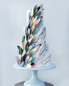 a multi - tiered cake decorated with colorful feathers on a blue stand against a gray background