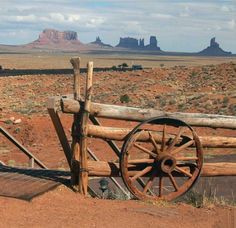 an old wooden wagon wheel leaning against a fence in the desert with mountains in the background