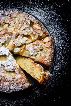 a pie with several pieces cut out and covered in powdered sugar on a black plate