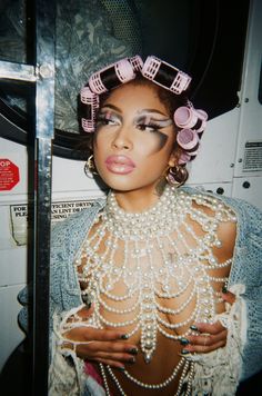 a woman with makeup and pearls on her head is posing in front of a bus