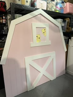 a pink barn shaped like a house with two chickens in the window and one door open