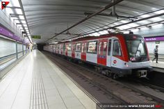 a red and white train pulling into a station next to a man standing on the platform