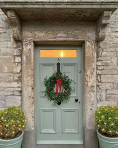 a green door with a wreath on it and two potted plants in front of it