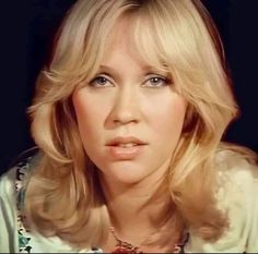 a woman with blonde hair and blue eyes wearing a floral shirt looking at the camera