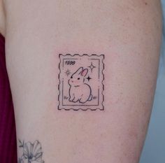 a small tattoo on the back of a woman's left arm, depicting a rabbit in a postage stamp