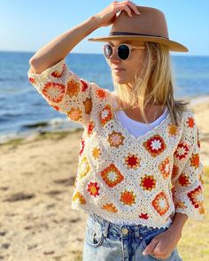 a woman standing on top of a beach next to the ocean wearing a hat and sunglasses