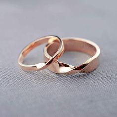 two wedding rings sitting on top of each other in front of a gray background,