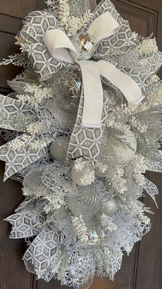 a christmas wreath with silver and white decorations hanging on a wooden door, decorated with ribbon